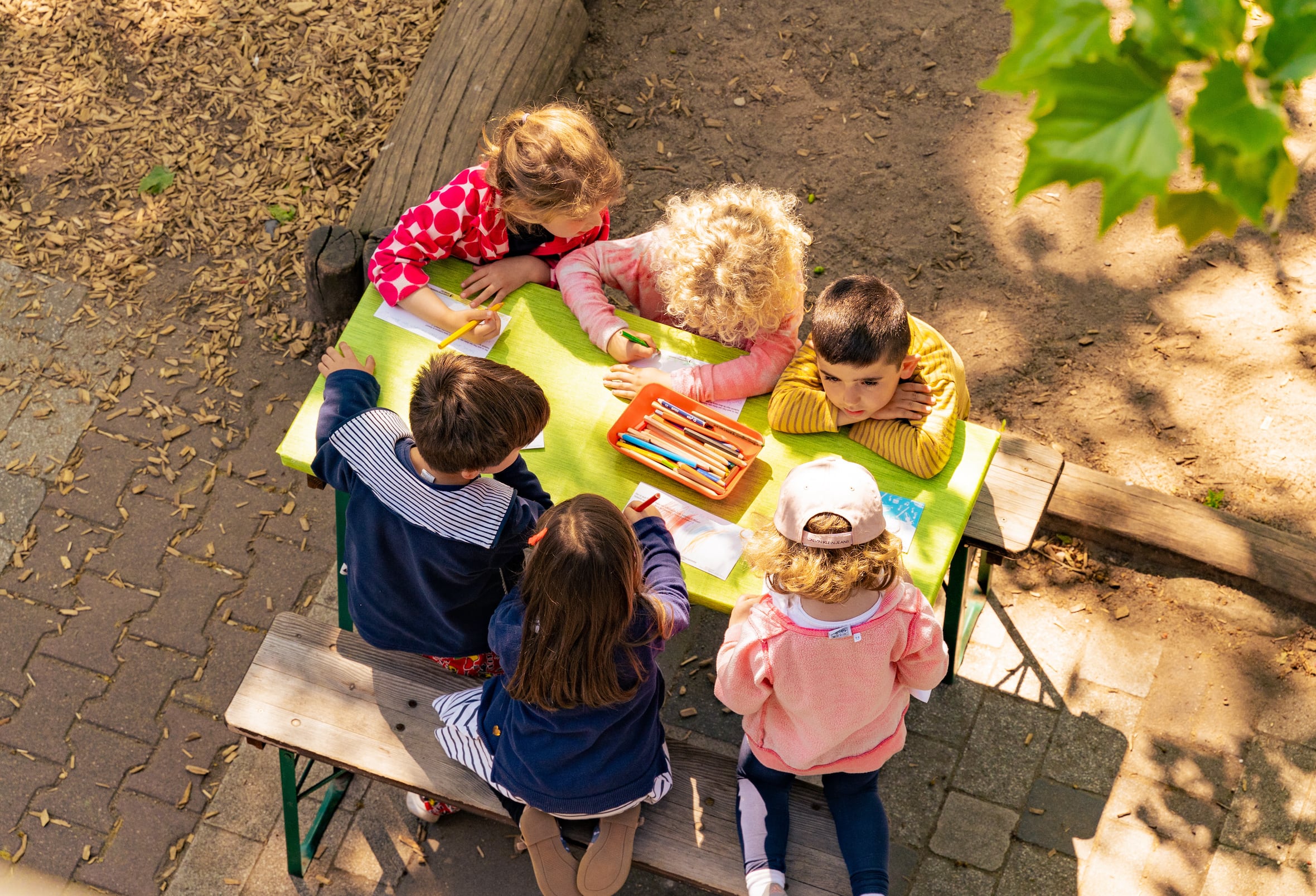 Kinder malen gemeinsam an einem Tisch auf dem Außengelände